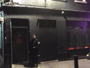 Dublin's best cocktail bars - Image of man dressed in black security clothes outside a building painted entirely black including boarded windows