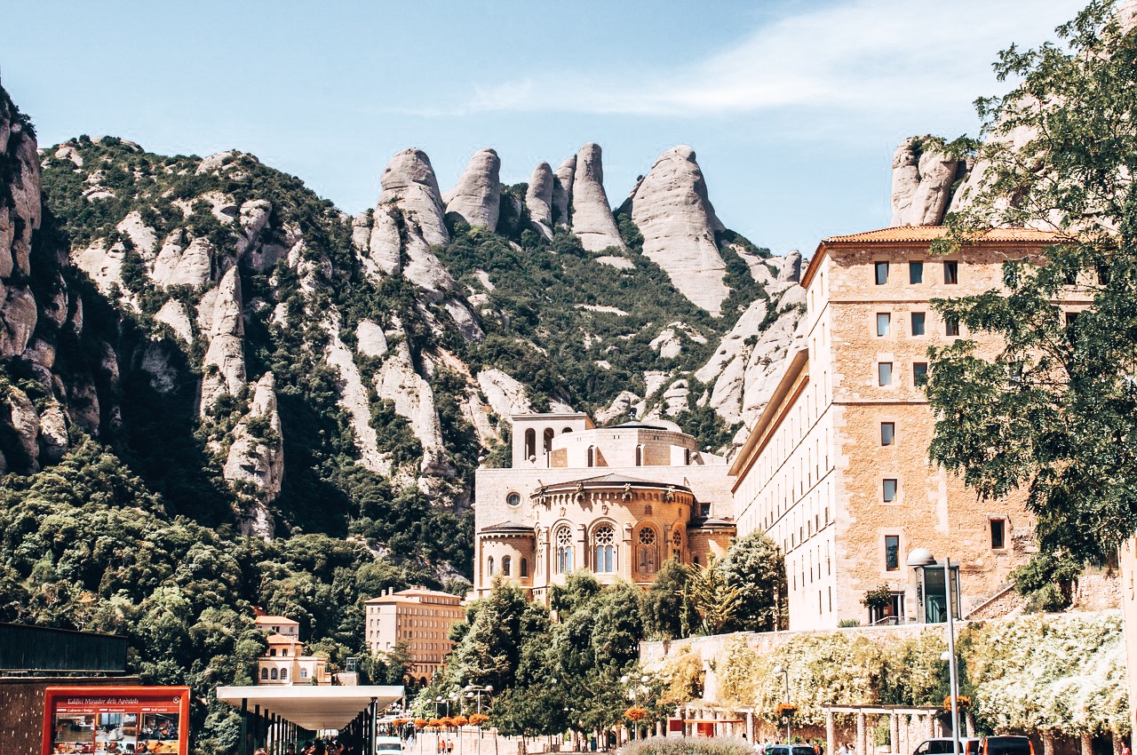 Amazing places to visit near Barcelona - Image of Montserrat - a Terracota building with mountains in the background