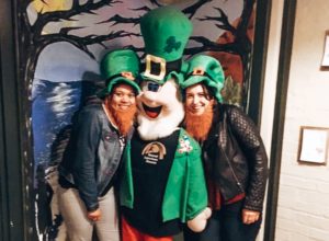 Two girls with green hats on posing with a leprechaun model