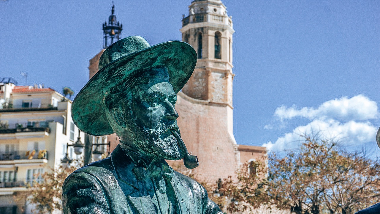 Amazing places near Barcelona - Sitges - A statue of man smoking a pipe with church steeple in the background