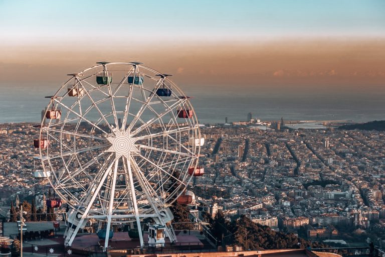 Rainbow coloured ferris wheel on top of a cliff overlooking Barcelona city