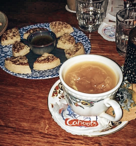 Unique Themed Cocktail Bars in London - Cocktail served in a traditional tea cup and saucer with a plate of buttered crumpets