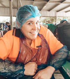 88 days of farm work - Girl smiling at camera with hair net and plastic apron and arm protectors on