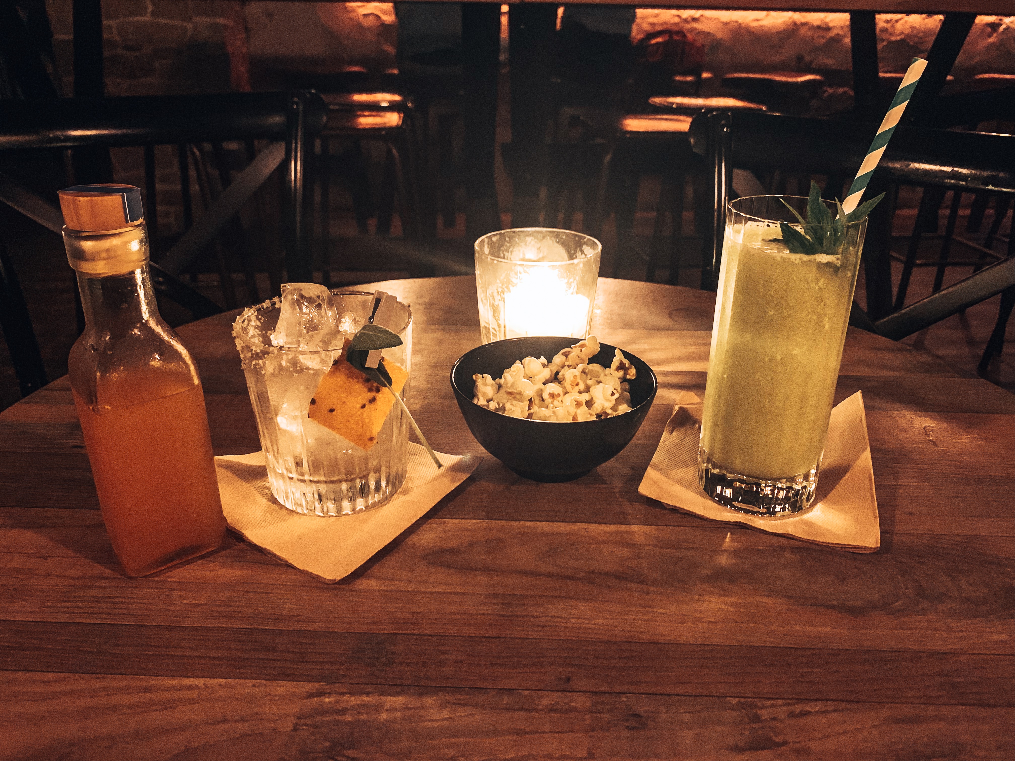Cocktails on a candlelit table with a small bowl of popcorn