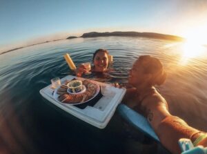 Two girls enjoying a tray of snacks whilst floating in a lake during sunset