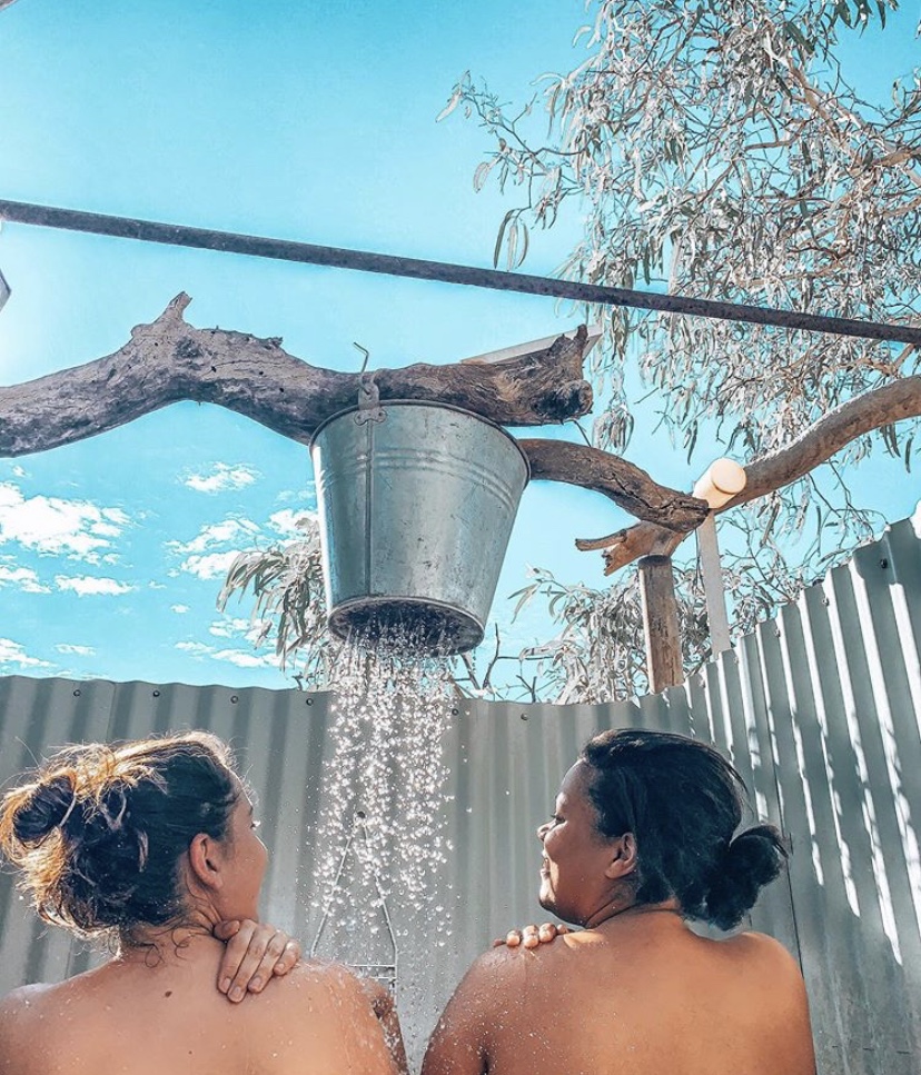 Two girls showering outside under a bucket shower