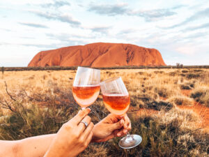 Uluru - Two wine glasses clinking with Uluru in the background