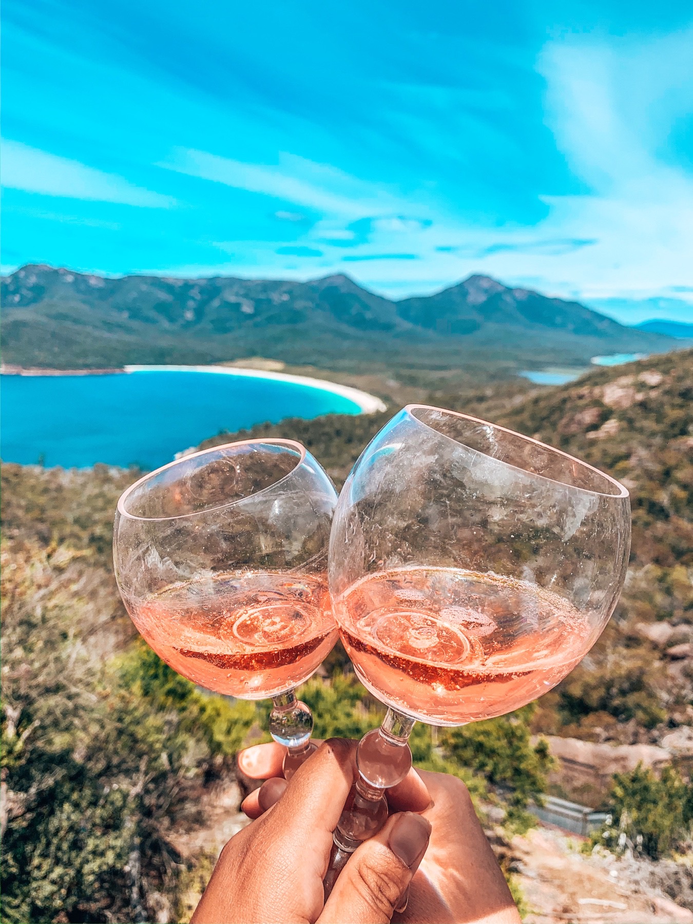 Freycinet WIne Glass Bay - Two wine glasses of Rosé clinking with wineglass bay visible through the glass - Lap of Tasmania