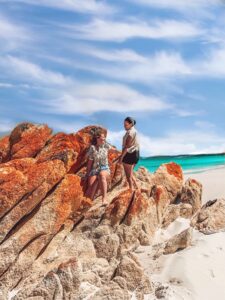 Bay of Fires Tasmania - Image of Two Girls Standing on burnt orange rocks overlooking the Ocean - Things To Do In Tasmania