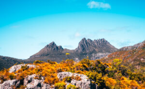 Cradle Mountain, Tasmania - Image of mountain range with orange and green bush in the forefront of the photo - Lap of Tasmania