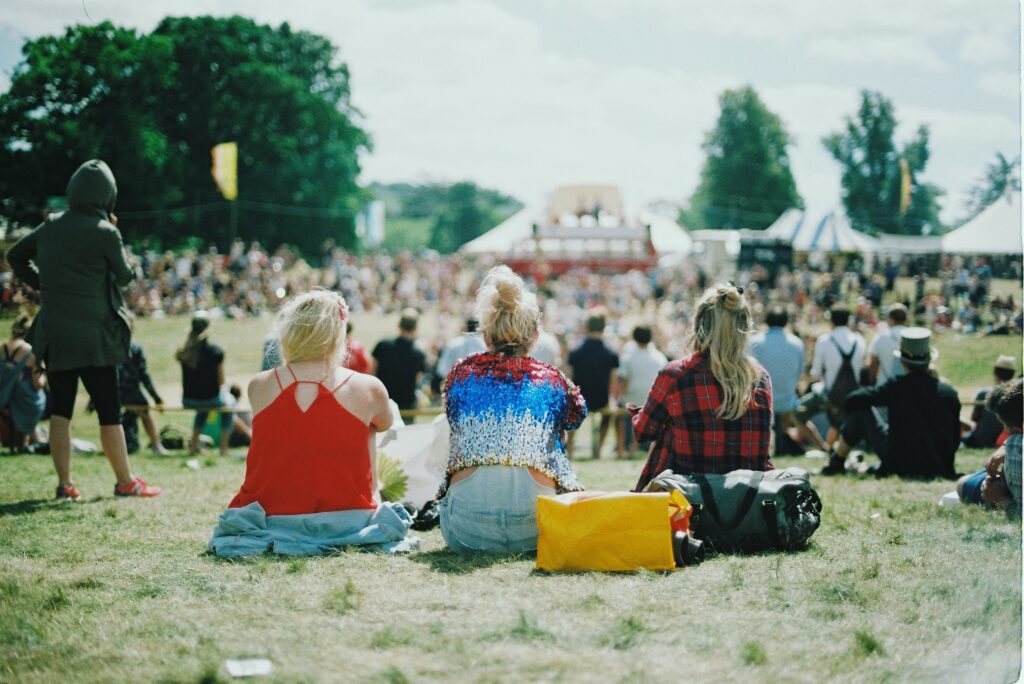 Three girls sitting in a crowded field of an affordable summer festival in the UK